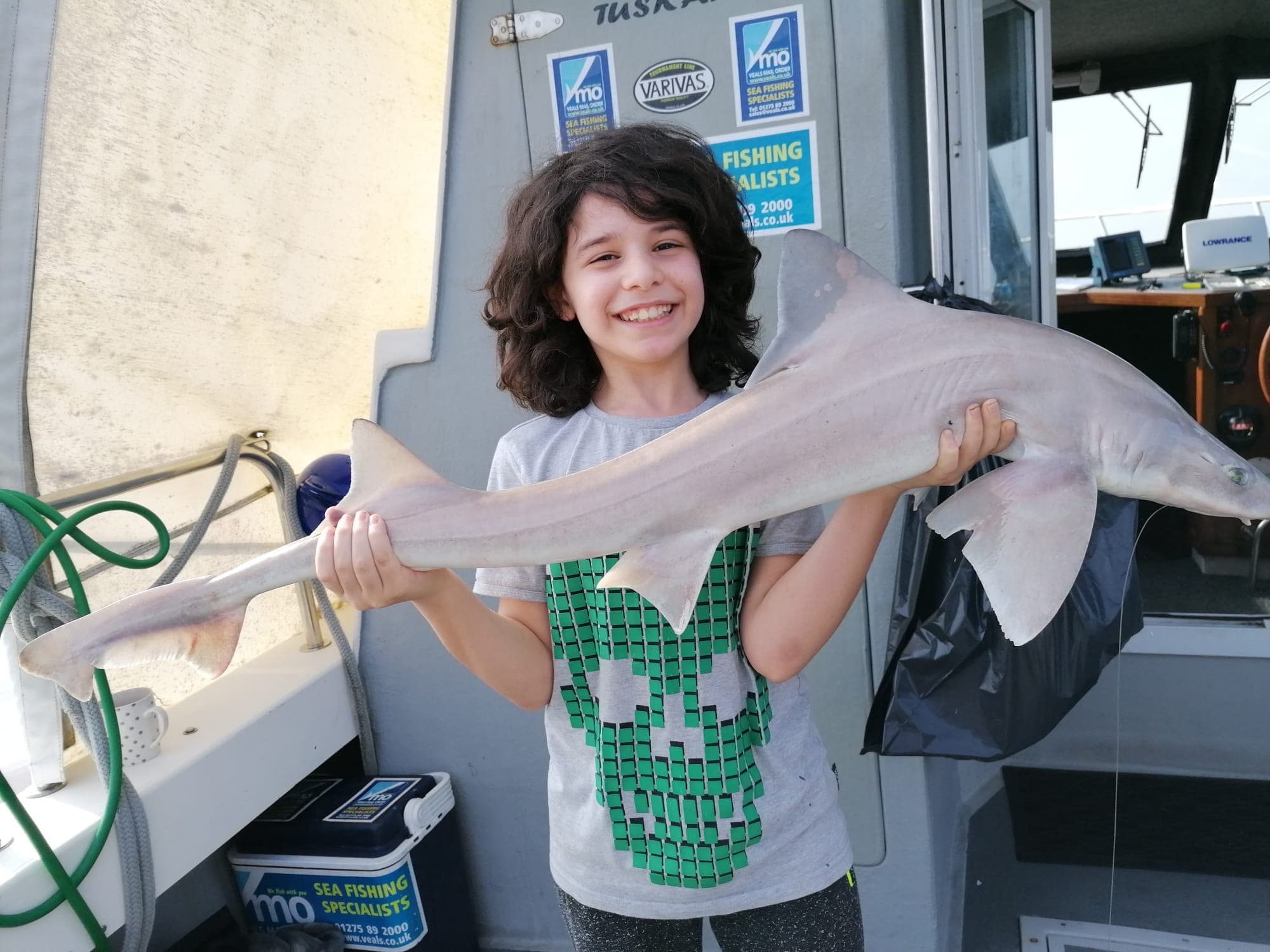 A young angler beaming with a smooth-hound on deck